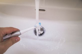 A bathroom tap is running while a toothbrush is held under the running water, symbolic image of