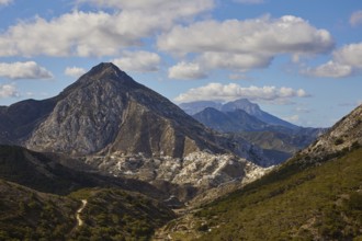 Mountain landscape with rocky peaks under a slightly cloudy sky, surrounded by green valley,