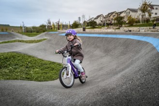 Child on pump track with bicycle helmet, riding bicycle on winding path on a cloudy autumn day,