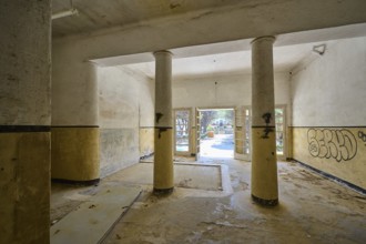 An abandoned corridor with columns, graffiti on the walls and daylight streaming in through the