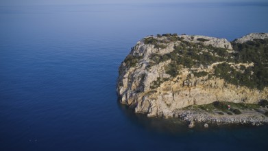 Drone shot, A rocky coastline with a rugged rocky outcrop bordered by calm sea and blue sky,