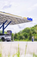 A charging station for electric cars with a car, green trees in the background and a slightly