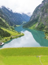 A peaceful mountain lake surrounded by mountains and forest under a cloudy sky, Stilluptal,