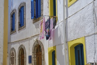 Colourful laundry hanging between houses with blue and yellow shutters and white walls, Platia,