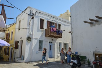 People standing outside an old white building with a balcony, laundry hanging outside, Mandraki,