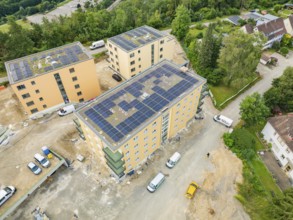 Aerial view of several buildings with solar panels on the roofs, surrounded by trees and green