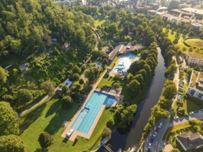 Spacious view of an outdoor swimming pool in the middle of a park, adjacent to a narrow river and