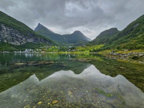 Mountainous landscape with a calm fjord reflecting the surrounding mountains and village,