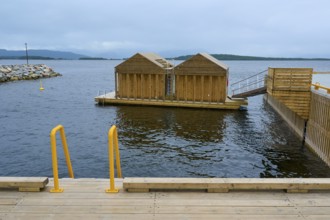 Outdoor sea pool by the fjord with small wooden sauna huts, overcast sky and calm water, Molde,