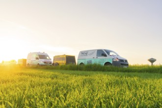 Transport vehicles on a green meadow at sunset with a clear sky, glass fibre installation, Calw