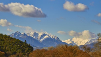 Clear view of snow-capped mountains behind green hills under a blue sky, autumn foliage colouring,