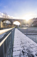 Wooden walkway with snow under a viaduct at dusk, with clear sky and bright light, forest ball from