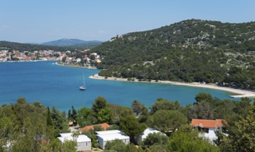 Coastal town with pine trees and sailing boats, surrounded by blue sea, bay near Tisno,