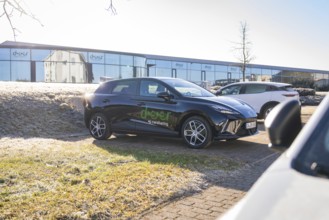 Black car in a car park in front of modern office buildings in sunny weather, Deer E- Carsharing