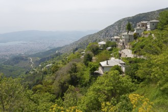 Mountain landscape with scattered houses on a green slope and a wide view of the town of Volos in