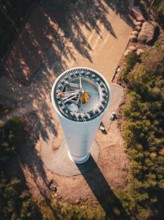 A tall wind turbine under construction, surrounded by forest and autumn atmosphere seen from above,