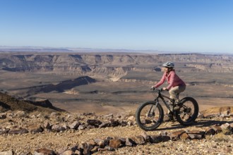 Woman riding a mountain bike, fatbike, on the edge of the abyss, behind the gorge landscape of the