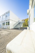 Container building with access stairs and autumn forest in the background, under a clear sky,