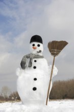 Decorated snowman with carrot nose, hat, pipe, scarf and broom in the snow in winter