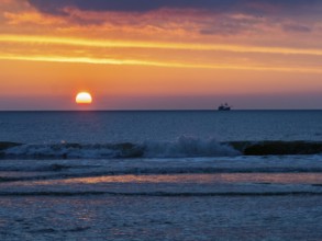 Silhouette of a fishing boat against a colorful sunset over the North Sea, and waves breaking on