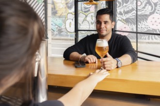 A man smiles as he receives a freshly poured beer from a bartender at the bar of a contemporary bar