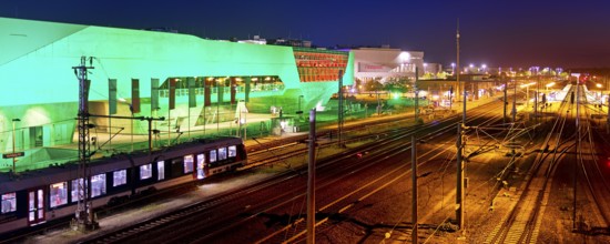 The colourfully illuminated phæno building and the main railway station with a local train at