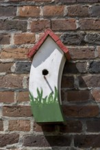 A colourful birdhouse with a plant motif on a brick wall in the sunlight, Münsterland, North