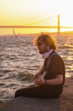 Hipster street musician in black playing electric guitar in the street on sunset on embankment with