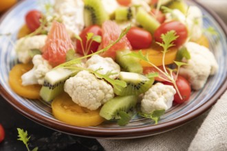 Vegetarian salad of cauliflower cabbage, kiwi, tomatoes, microgreen sprouts on black concrete