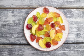 Various fruit jelly candies on plate on gray wooden background. top view, flat lay, close up