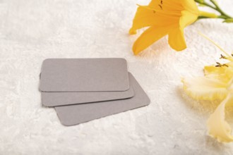 Gray paper business card mockup with orange day-lily flower on gray concrete background. Blank,