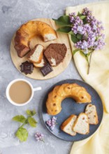 Cakes with raisins and chocolate and a cup of coffee. lilac flowers on a gray concrete background,