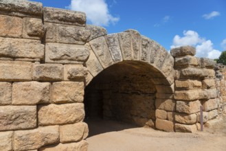 Historic stone archway from Roman times, surrounded by thick stone walls under a blue sky, Mérida,