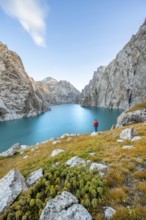 Young man at the turquoise mountain lake Kol Suu with rocky steep mountains, Kol Suu Lake, Sary