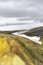 Two hikers on a hill in the distance, colourful volcanic landscape with hills and snow, Laugavegur