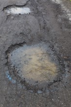 Potholes filled with rainwater on wet black asphalt road surface in spring, Montreal, Quebec,