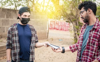 Side view of young man giving a surgical mask to another person, concept of a person giving a