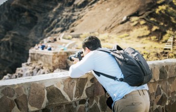 A tourist man with a photo camera taking photos at a viewpoint. Adventurous man with his camera