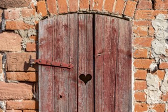 Weathered wooden door with heart to the loo, loo door, sandstone and brick façade, historic