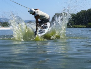 Young man jumping with wakeboard into the lake, water sports, water skiing in wakepark, Stráž pod