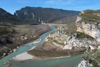 A winding river cuts through rocky landscapes and green hills, surrounded by steep mountains under