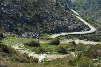 A winding path runs through a hilly and green landscape with rocky elevations, old Roman road, at