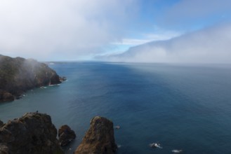 Steep cliffs jut into the blue sea under a cloudy sky, fog, Cape Cabo da Roca, westernmost point of