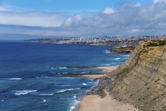 A coastal landscape with cliffs and a city visible in the background under a blue sky, Praia da