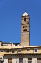 High historical tower in front of a blue sky with residential buildings in the foreground, church,