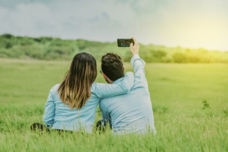 Couple in love taking a selfie sitting in a beautiful field. Young happy couple taking a selfie