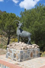 Bronze ibex statue on a brick base surrounded by green trees, Área Recreativa de Sedella, Parque