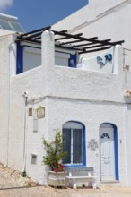 White and blue Mediterranean house with flowers in front of a terrace under a clear sky, Albufeira,