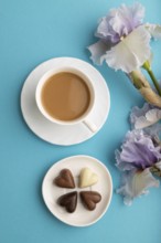 Cup of cioffee with chocolate candies and lilac iris flowers on blue pastel background. top view,