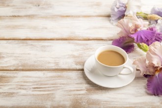 Cup of cioffee with lilac and purple iris flowers on white wooden background. side view, copy